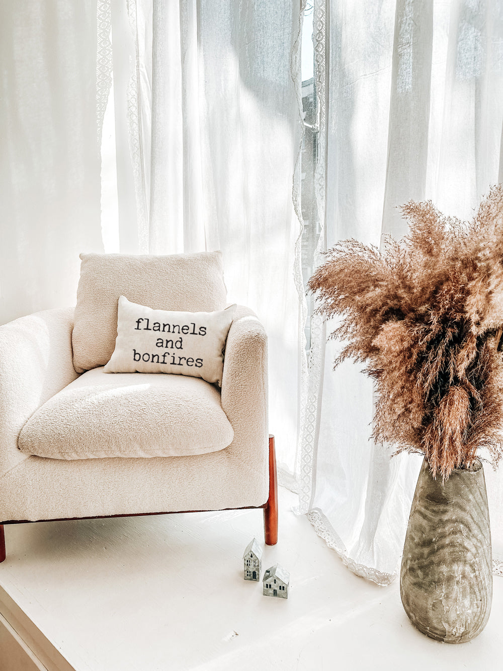 a cream chair with a fall pillow that says flannels and bonfires in a typewriter style font.